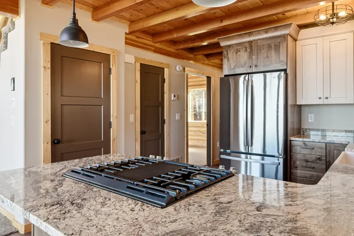 Kitchen featuring light stone counters, freestanding refrigerator, hanging light fixtures, black gas cooktop, and a wooden ceiling with exposed beams
