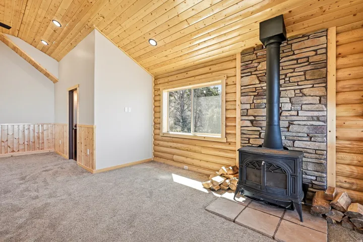 Unfurnished living room with log walls, carpet flooring, a vaulted wooden ceiling, a wood stove, and recessed lighting