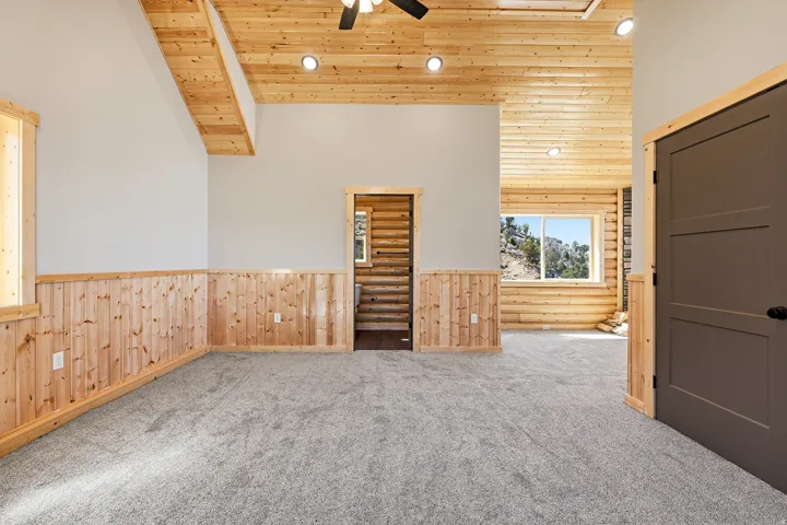 Spare room with a vaulted wooden ceiling, ceiling fan, carpet, wooden walls, and wainscoting