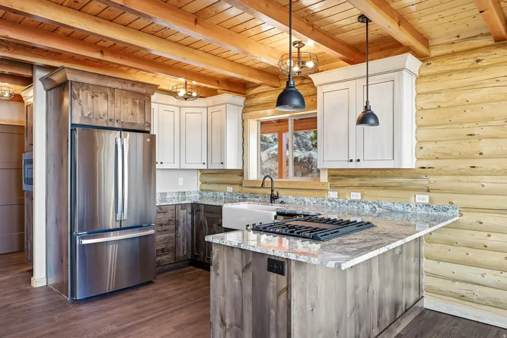 Kitchen featuring light stone countertops, stainless steel appliances, log walls, dual tone cabinetry, and a wood ceiling with exposed beams