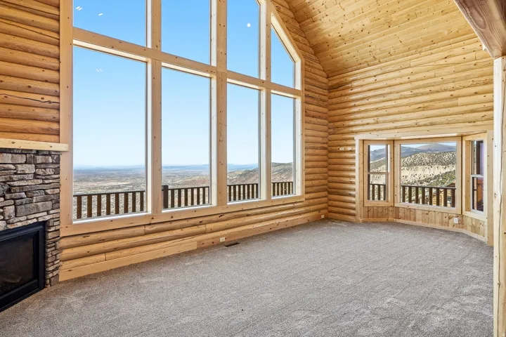 Unfurnished sunroom featuring rustic walls, a mountain view, carpet floors, and a vaulted wooden ceiling