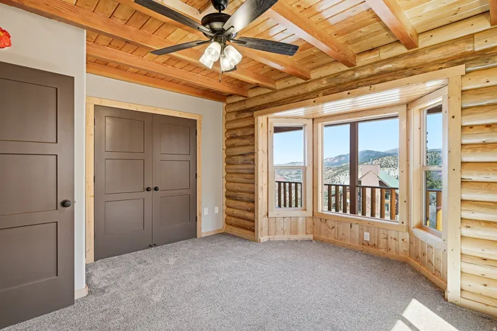 Unfurnished bedroom with log walls, a wood ceiling with exposed beams, a mountain view, light colored carpet, and a closet