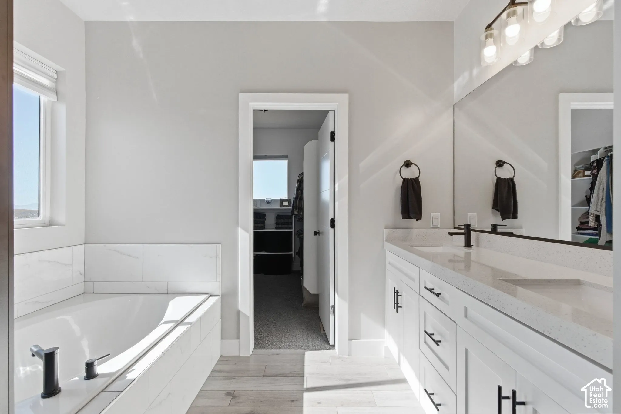 Full bathroom with double quartz vanity, a relaxing soaking tub, and titled shower