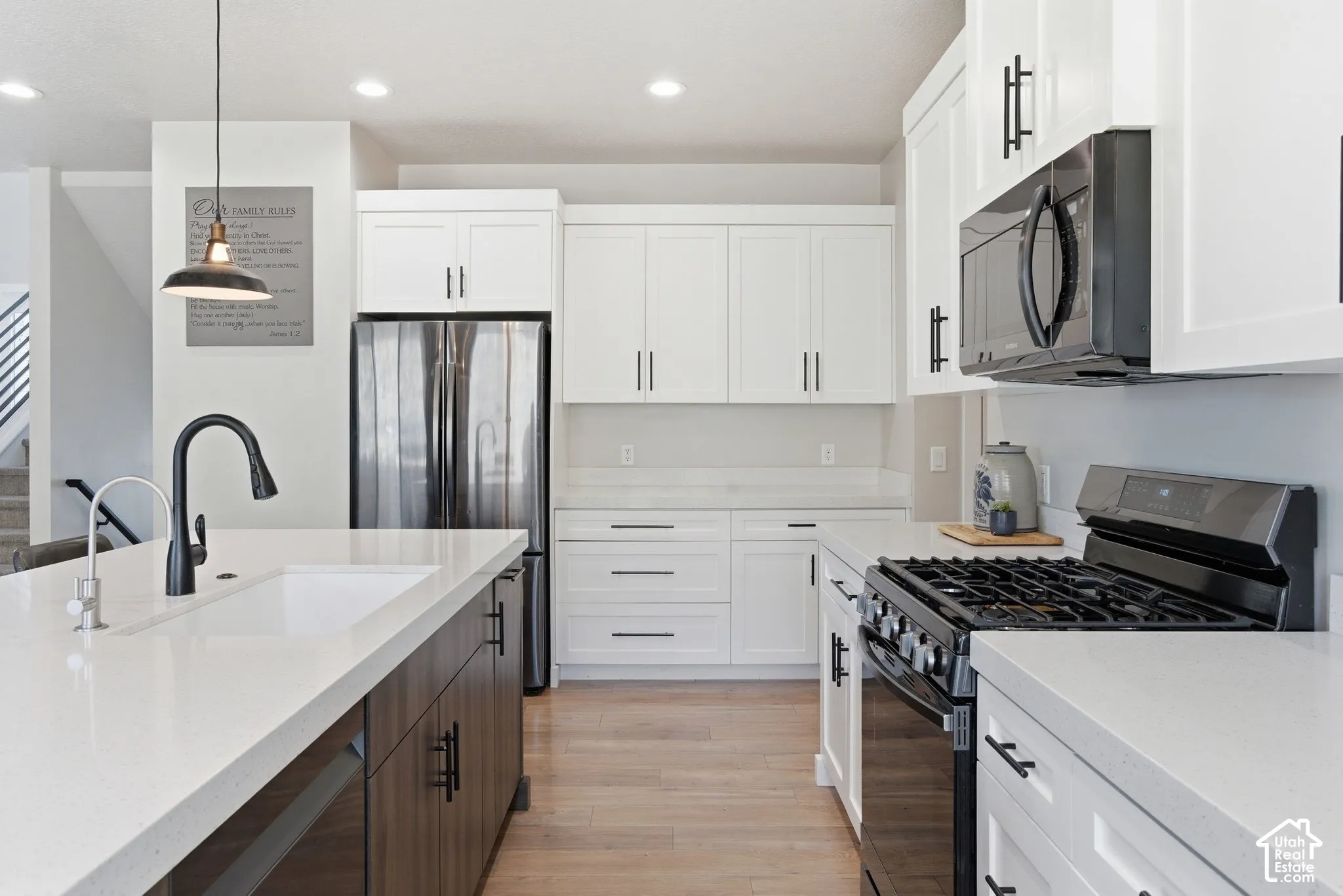 Kitchen with stainless steel appliances, dual tone cabinets, light stone counters, decorative light fixtures, and light wood-style floors