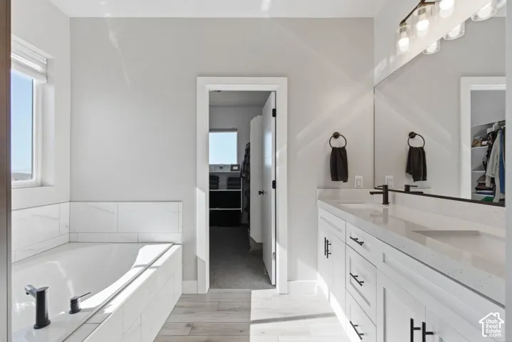 Full bathroom with double quartz vanity, a relaxing soaking tub, and titled shower
