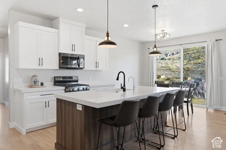 Kitchen featuring a large quartz island with sink, dual tone cabinetry, a kitchen breakfast bar, stainless steel appliances, and light wood finished floors