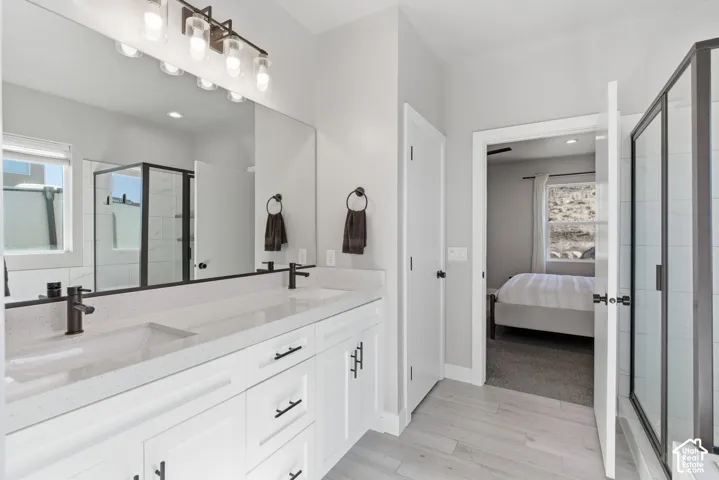 Ensuite bathroom featuring a shower, double vanity, and light wood-style flooring