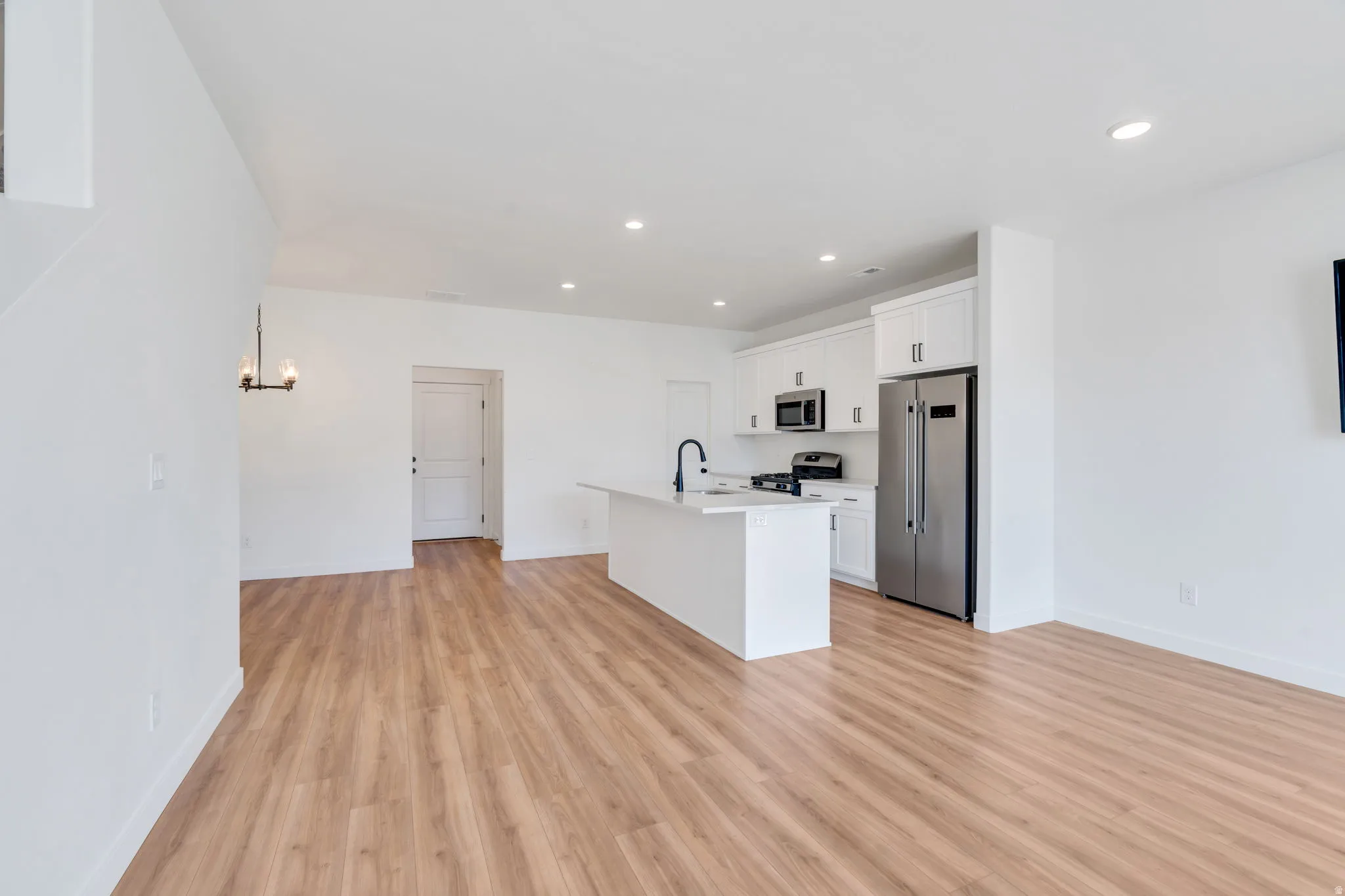 Kitchen featuring stainless steel appliances, white cabinetry, an island with sink, light wood-style floors, and open floor plan