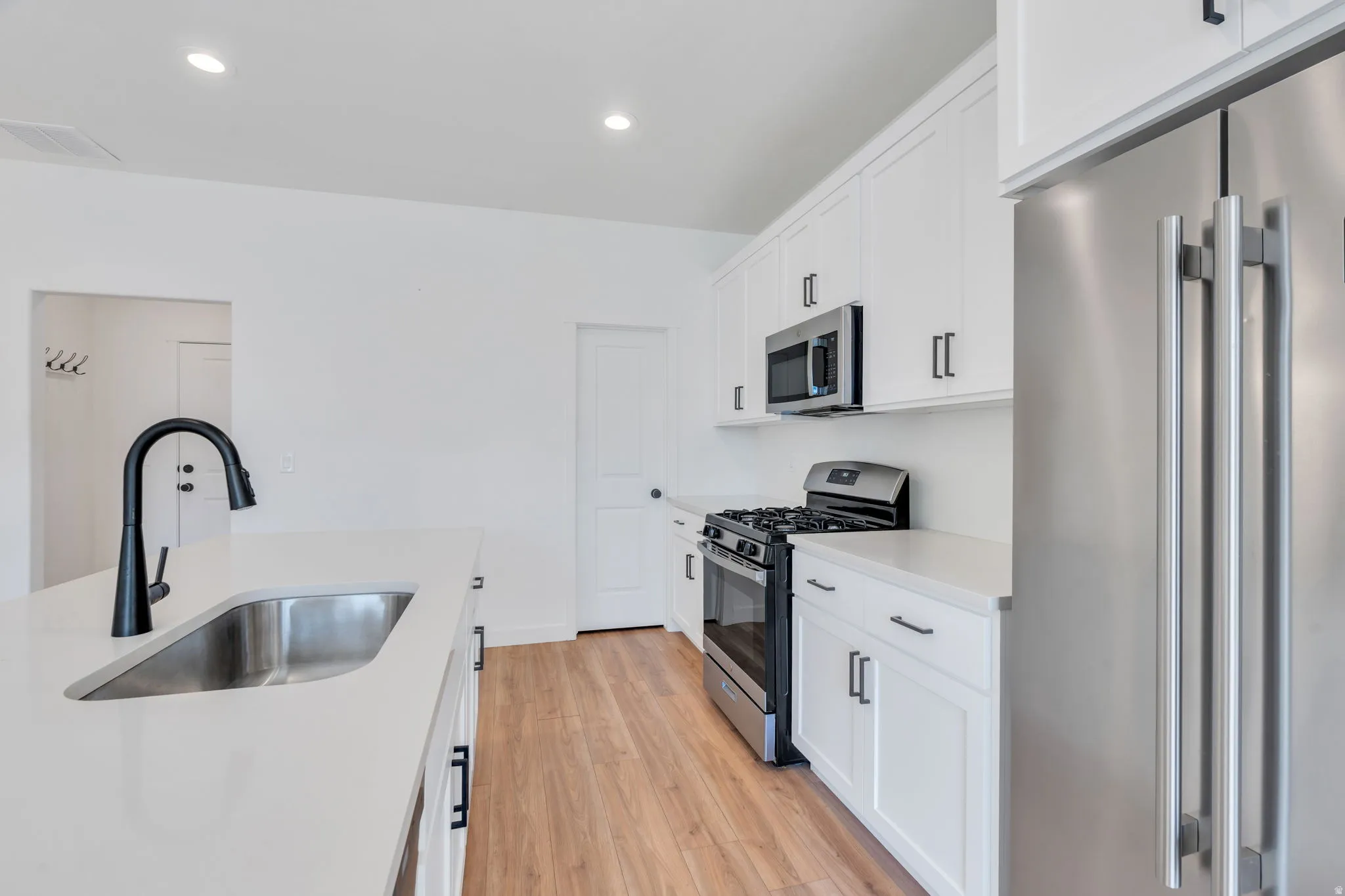 Kitchen with stainless steel appliances, light wood-type flooring, white cabinets, and recessed lighting