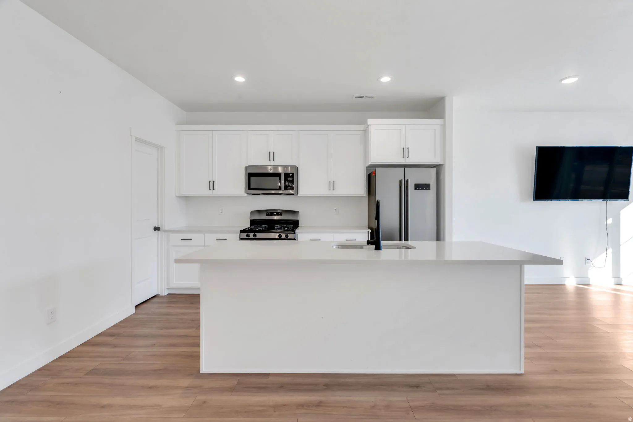 Kitchen with white cabinets, stainless steel appliances, light wood finished floors, a center island with sink, and recessed lighting