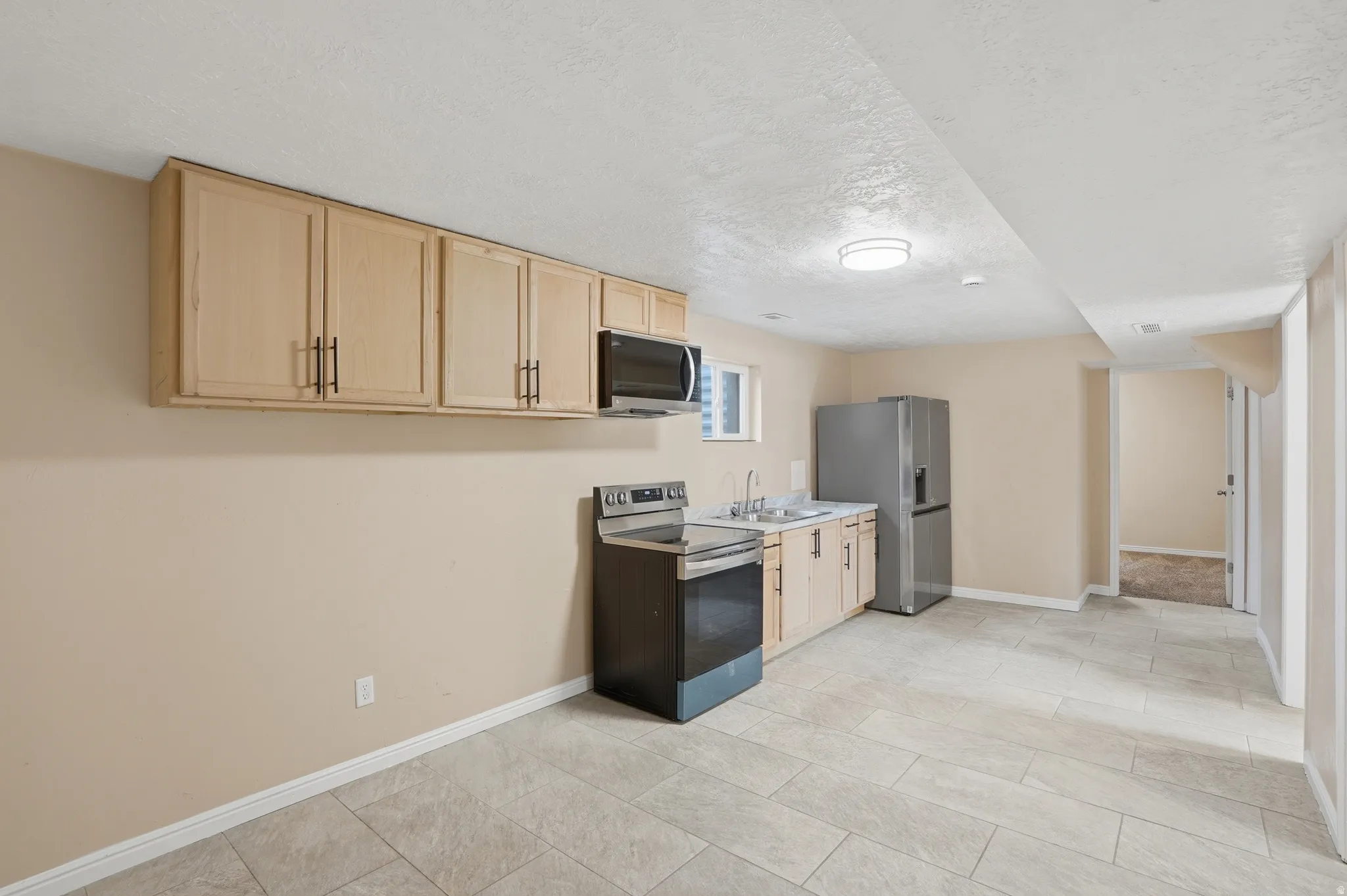 Kitchen with light wood finish cabinets, stainless steel appliances, a textured ceiling, and light countertops