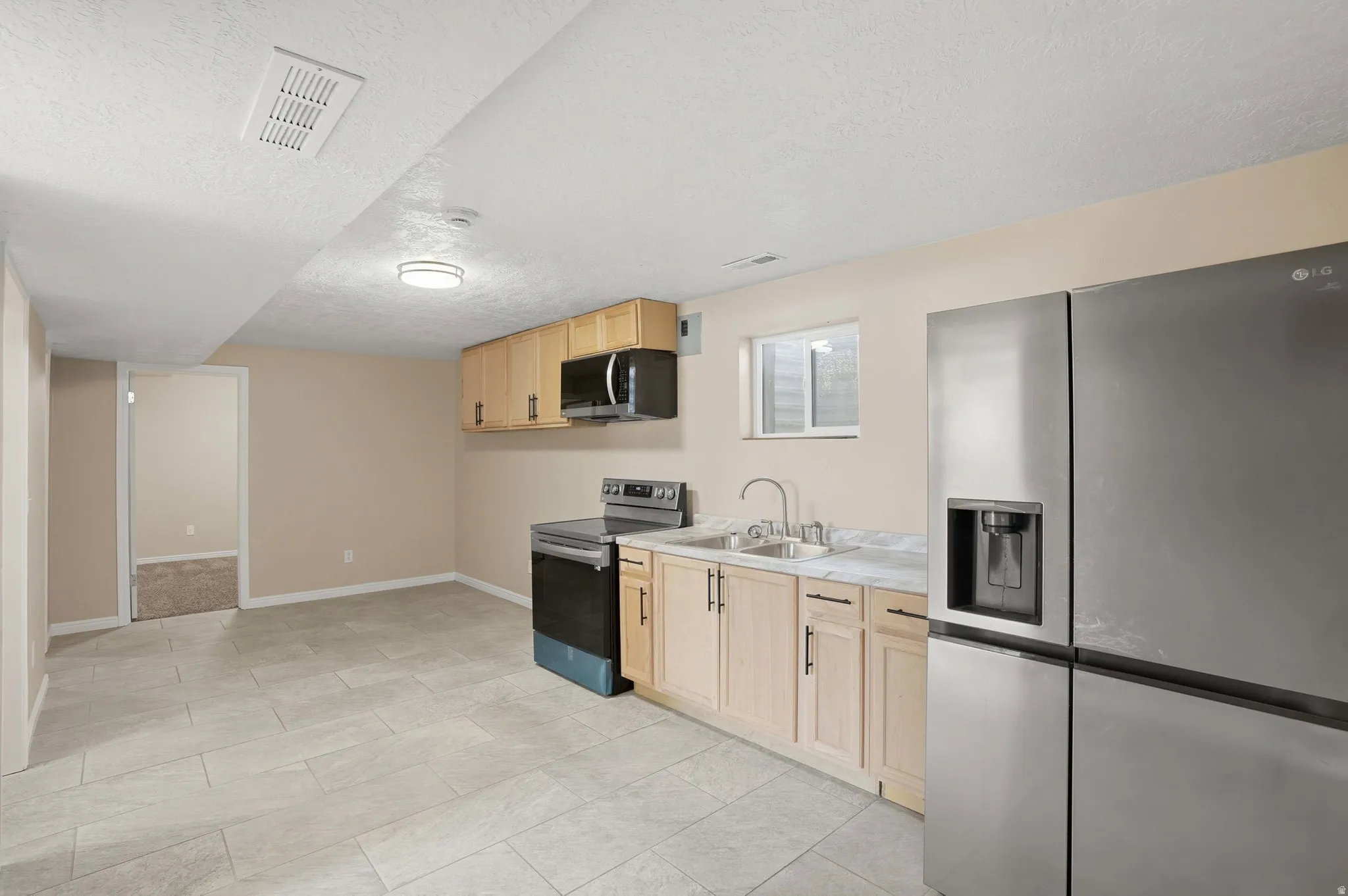 Kitchen with stainless steel appliances, light wood finish cabinets, a textured ceiling, and light countertops
