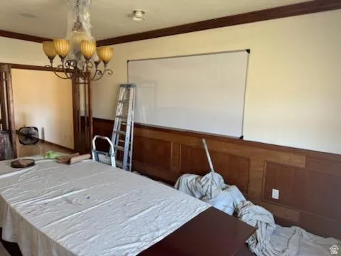 Bedroom with a wainscoted wall, hanging lights, crown molding, and wood walls