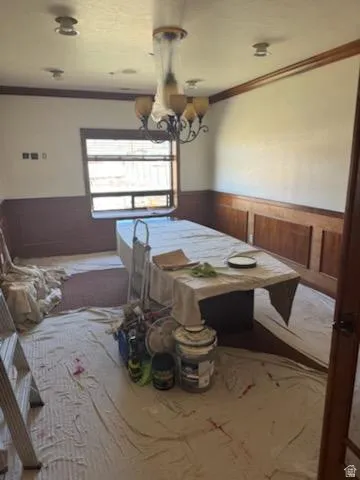 Dining room with a wainscoted wall, ornamental molding, wood walls, and suspended lighting