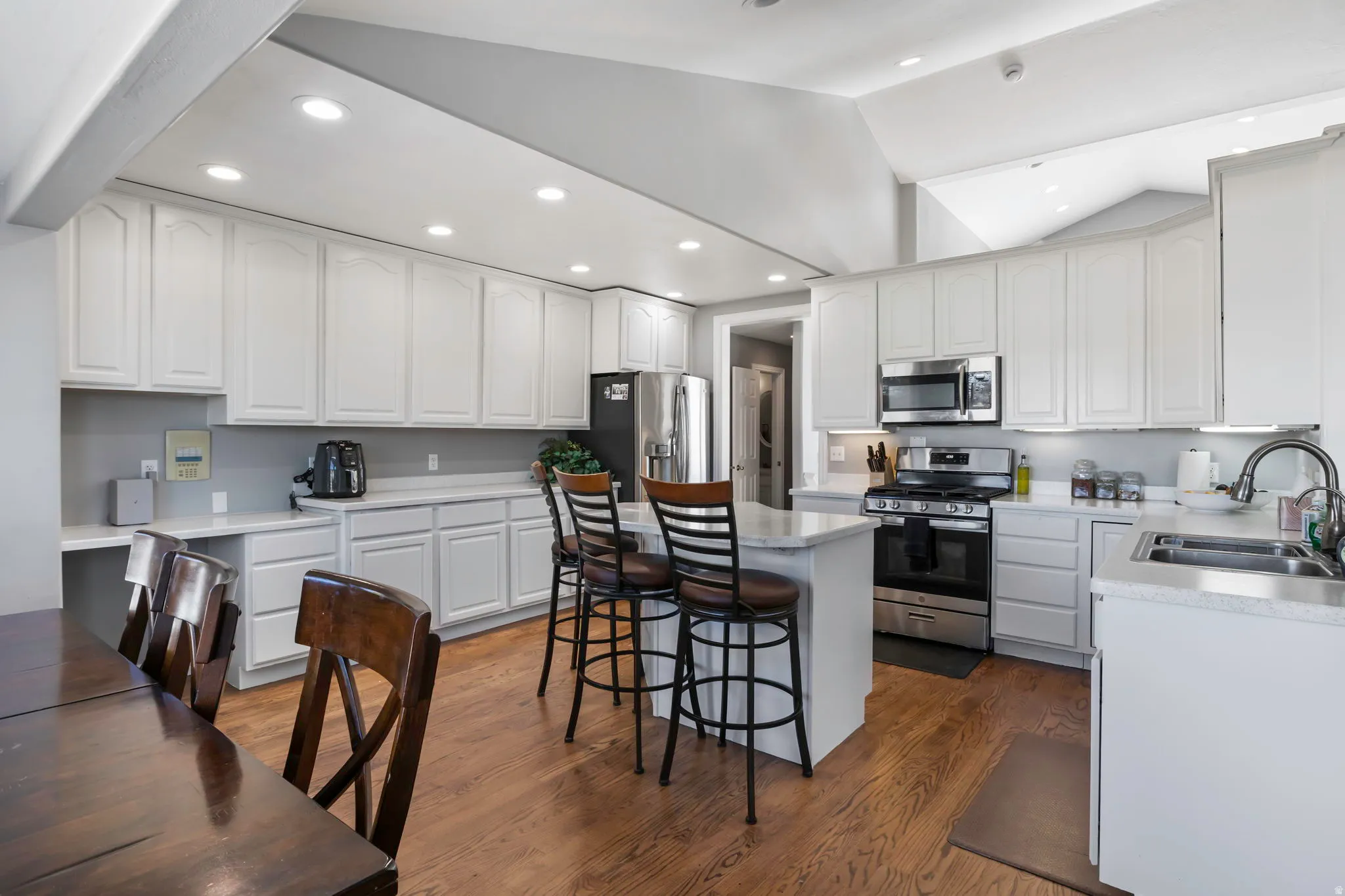 Kitchen with stainless steel appliances, lofted ceiling, a breakfast bar area, light countertops, and white cabinetry