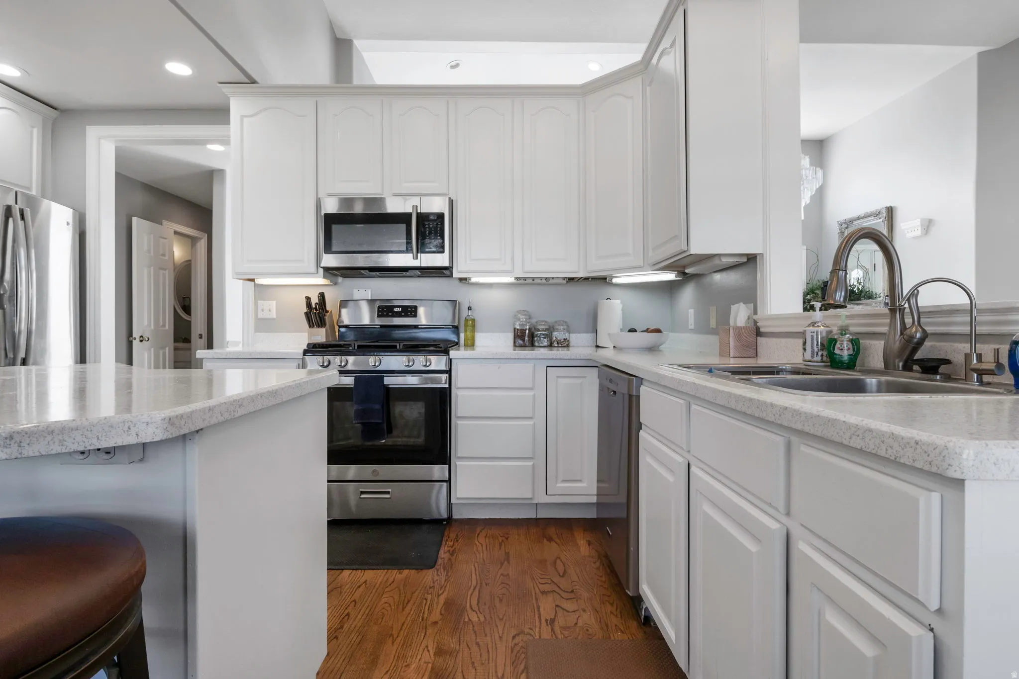 Kitchen featuring stainless steel appliances, white cabinets, a kitchen bar, dark wood finished floors, and recessed lighting