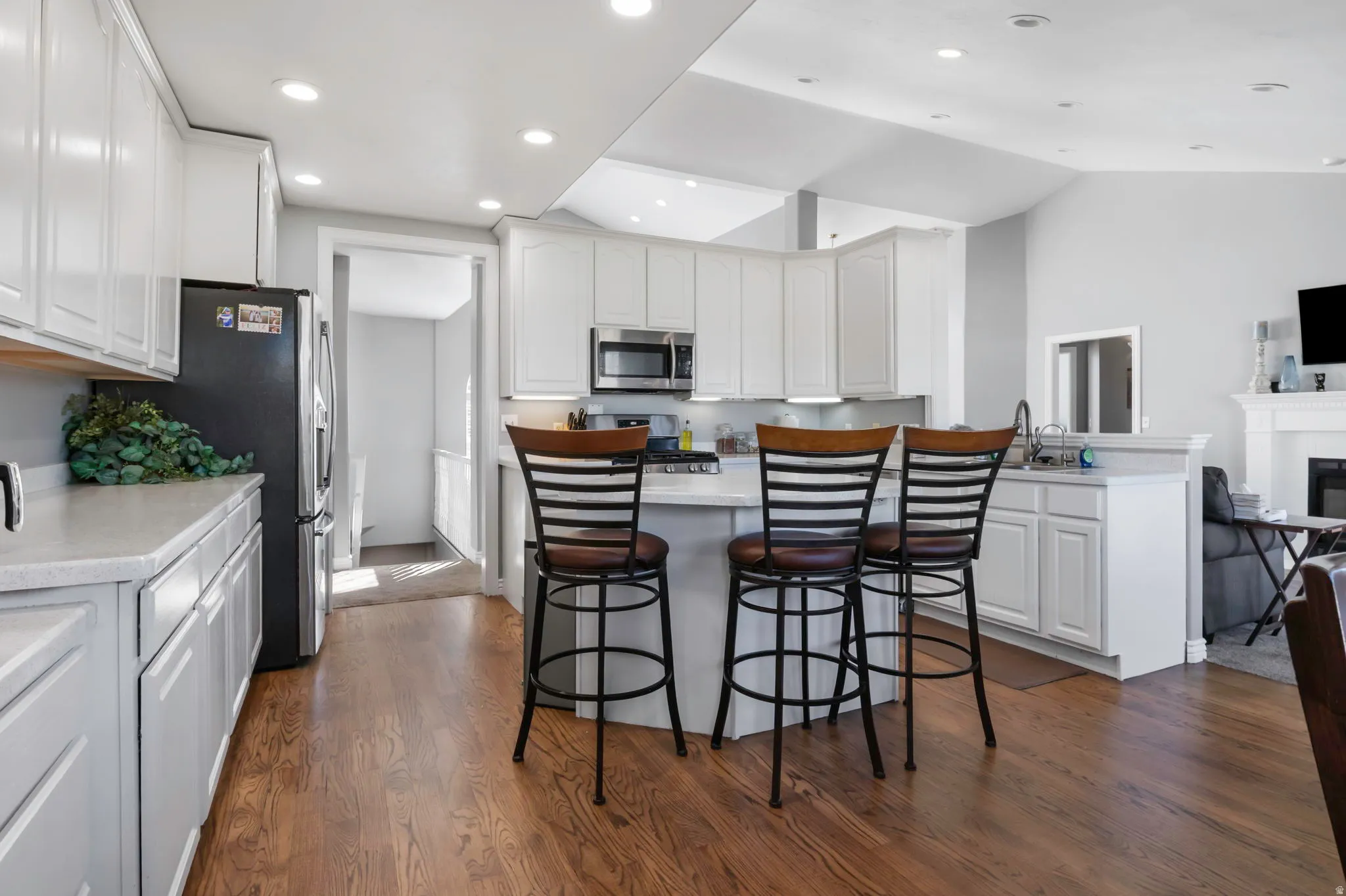 Kitchen with a breakfast bar, white cabinetry, dark wood-type flooring, stainless steel appliances, and recessed lighting