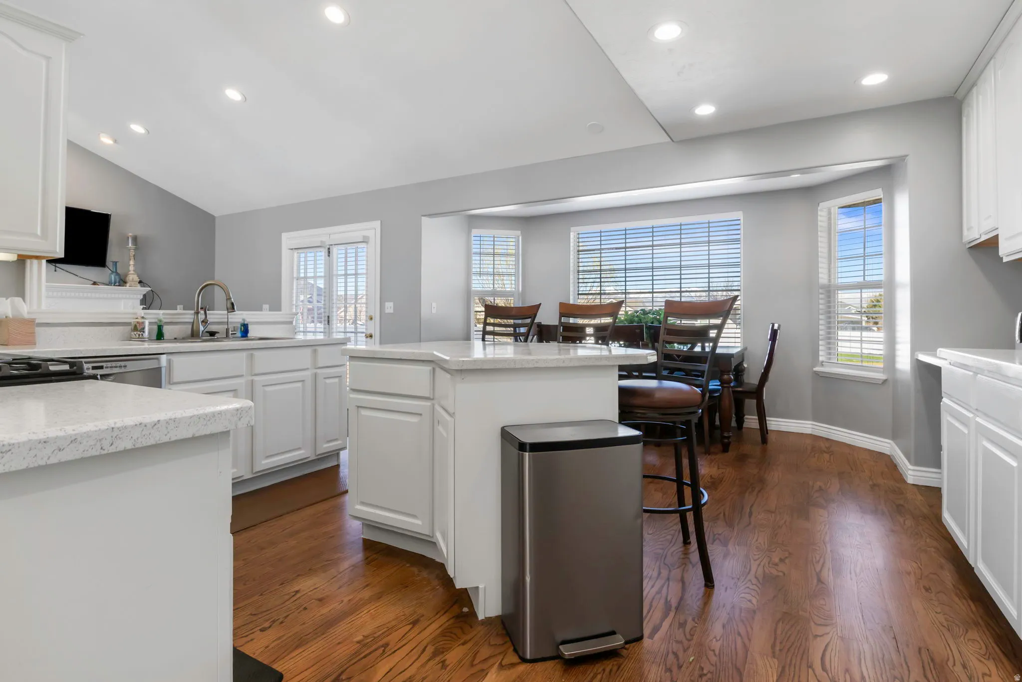 Kitchen with a kitchen breakfast bar, white cabinetry, a center island, dark wood-style flooring, and light stone counters