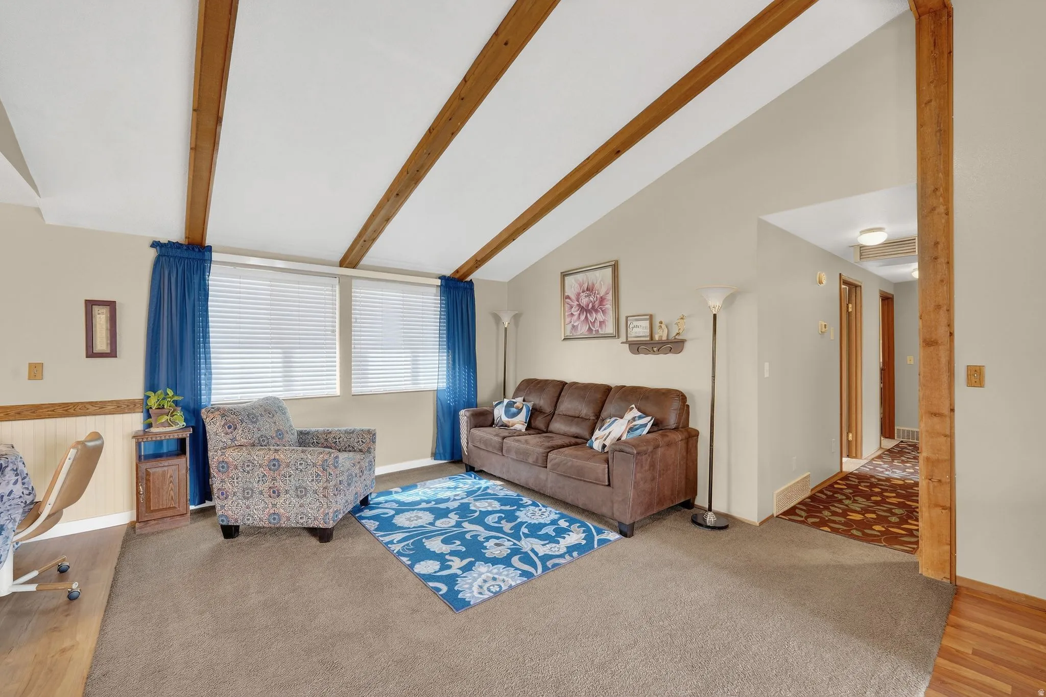 Living area featuring light colored carpet, vaulted ceiling with beams, and light wood-type flooring