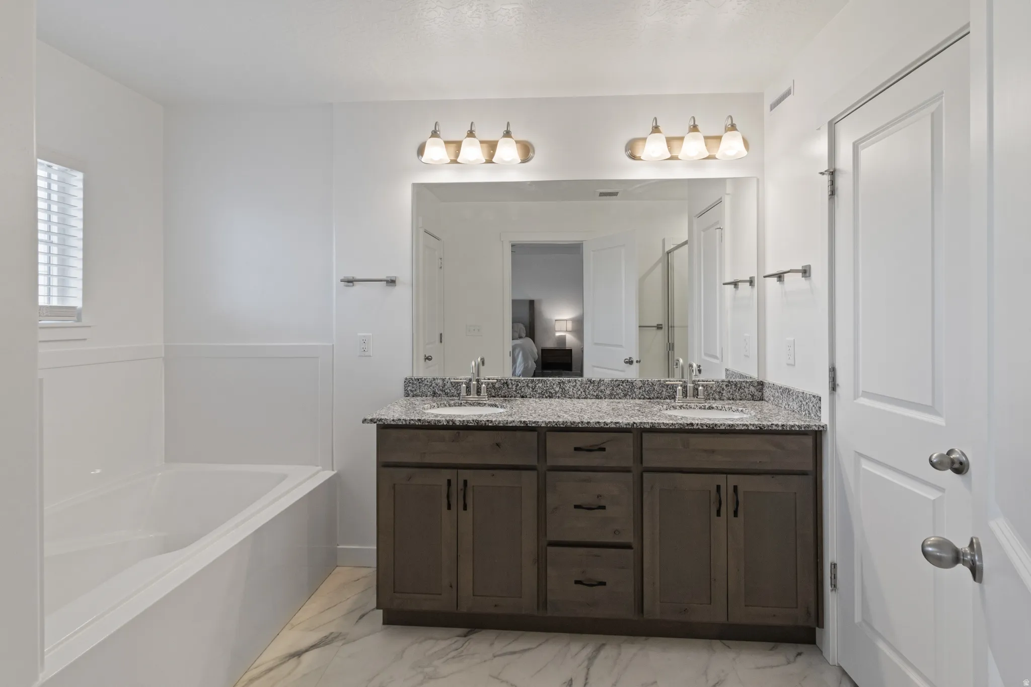 Ensuite bathroom with double vanity, a garden tub, and light marble finish floors