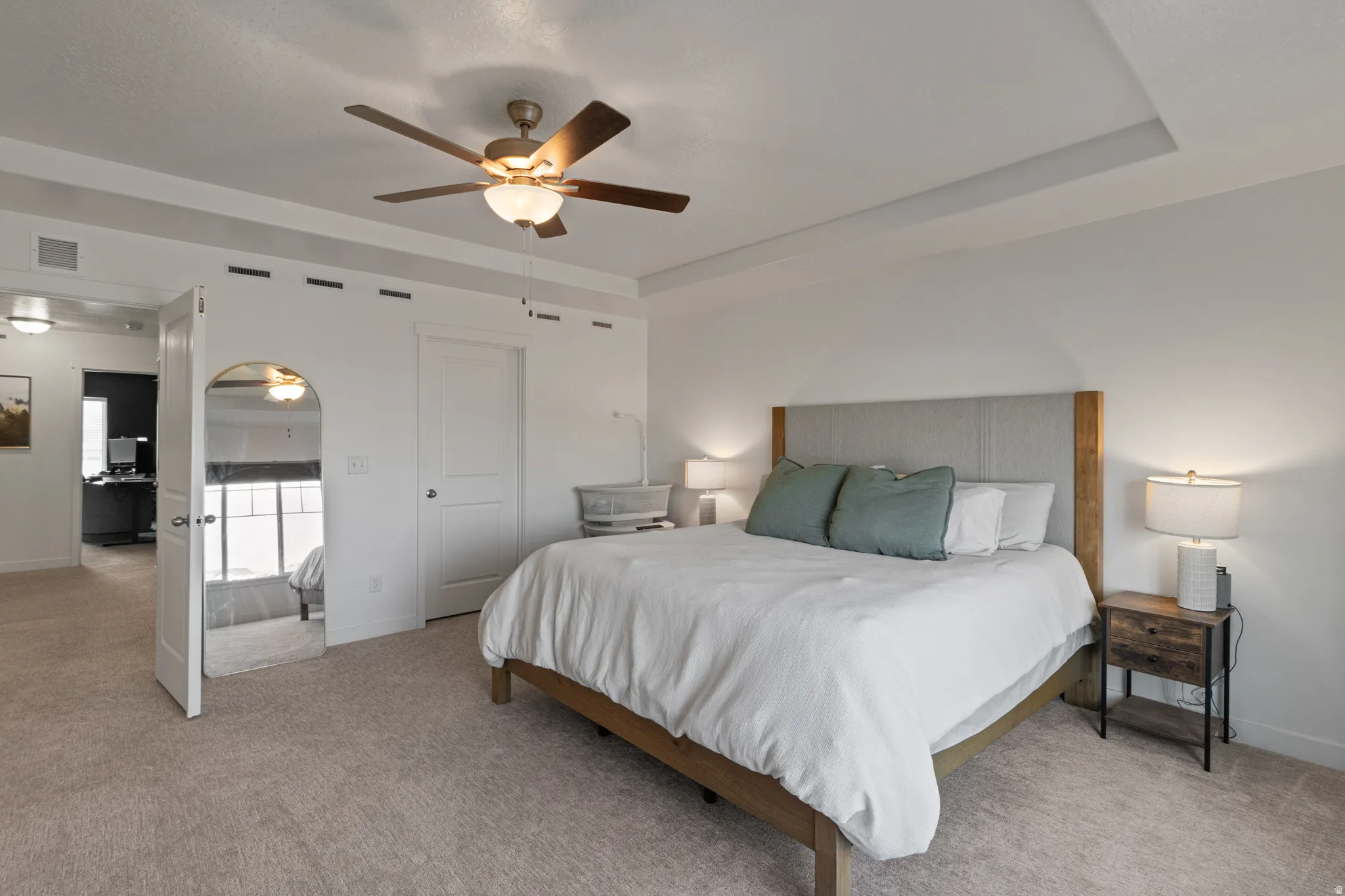 Bedroom with a tray ceiling, light colored carpet, arched walkways, and a ceiling fan