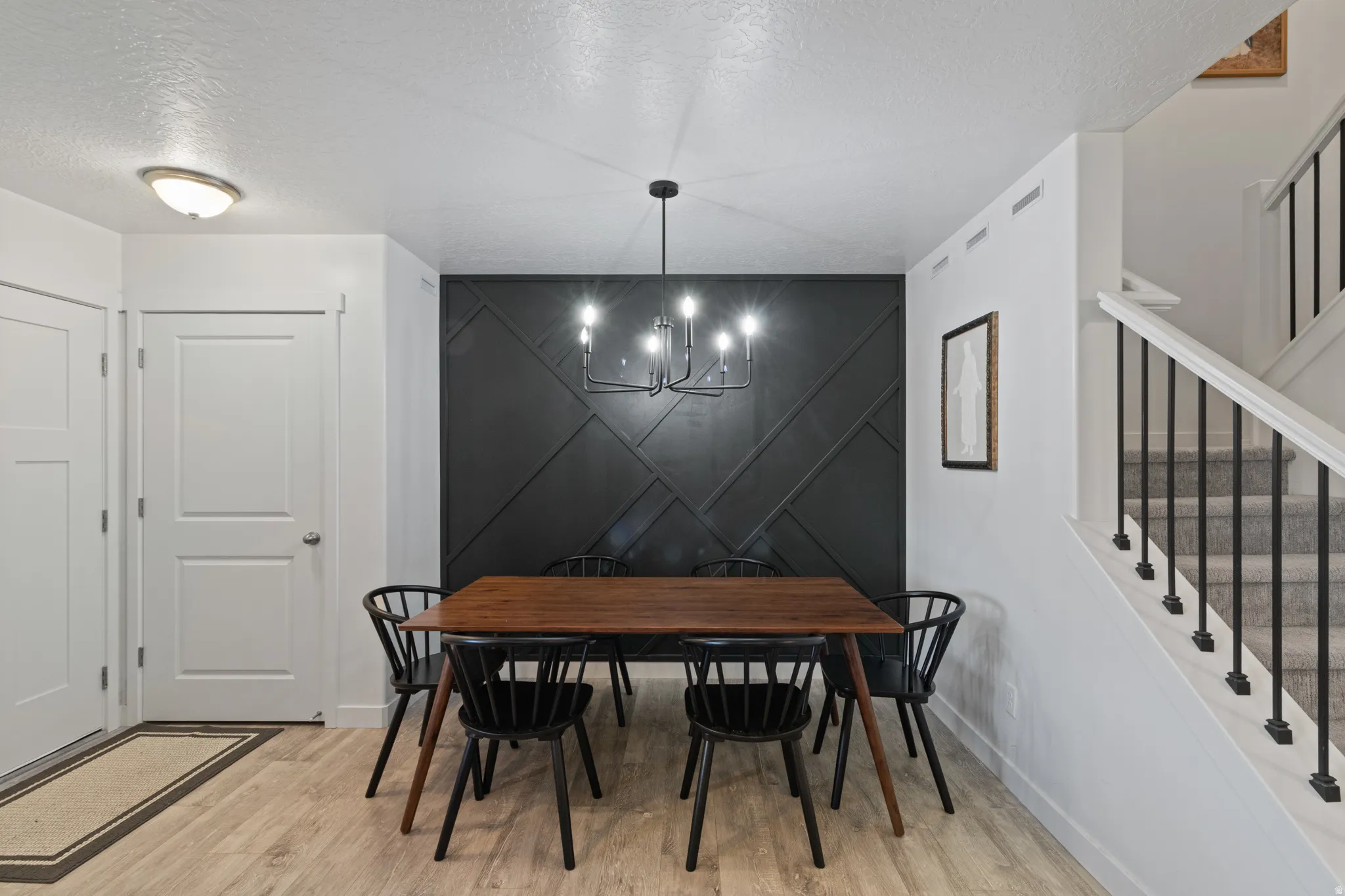 Dining room featuring an accent wall, a textured ceiling, a chandelier, light wood-style flooring, and a decorative wall
