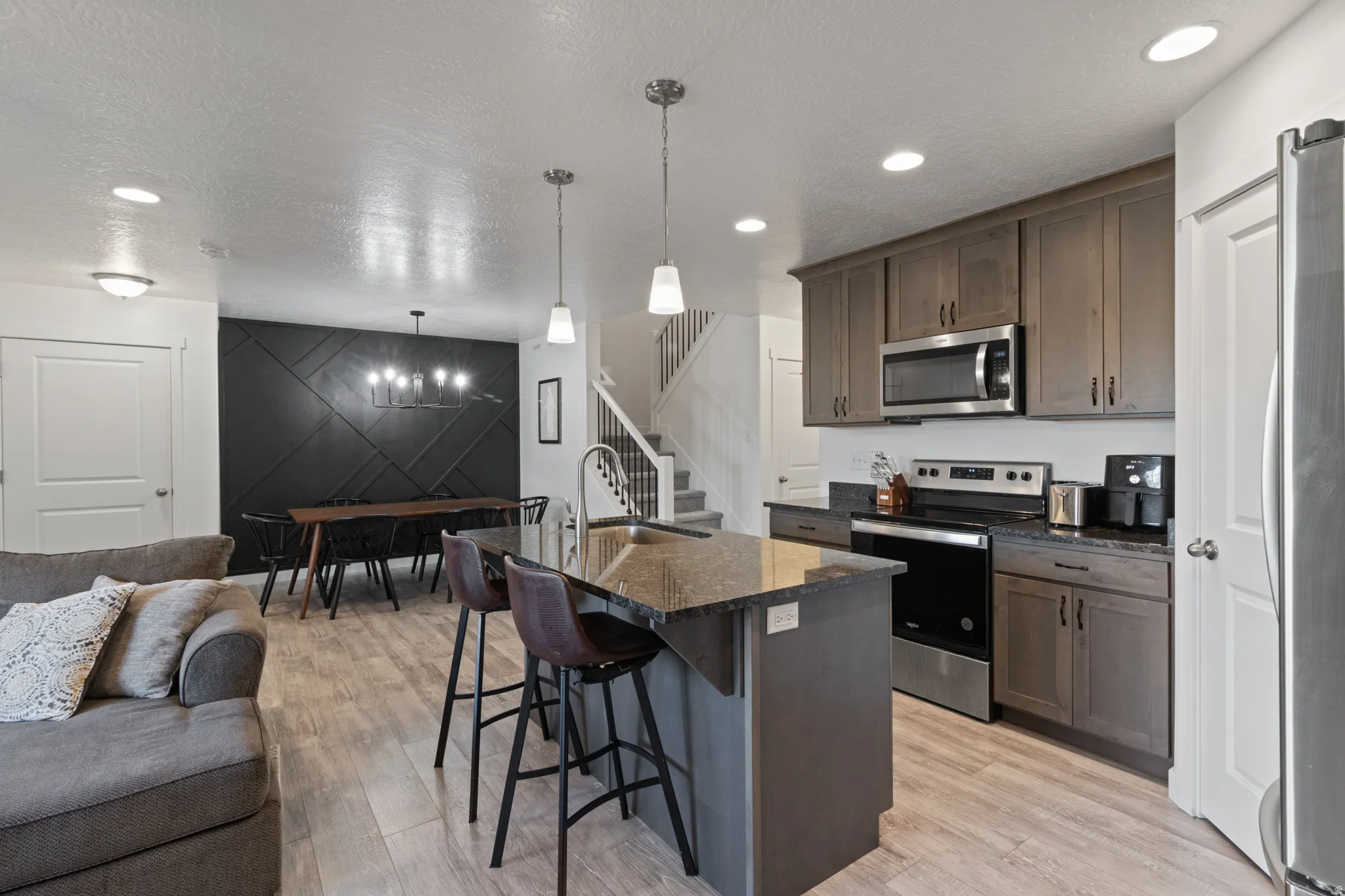 Kitchen featuring a breakfast bar, stainless steel appliances, open floor plan, a center island with sink, and dark stone counters