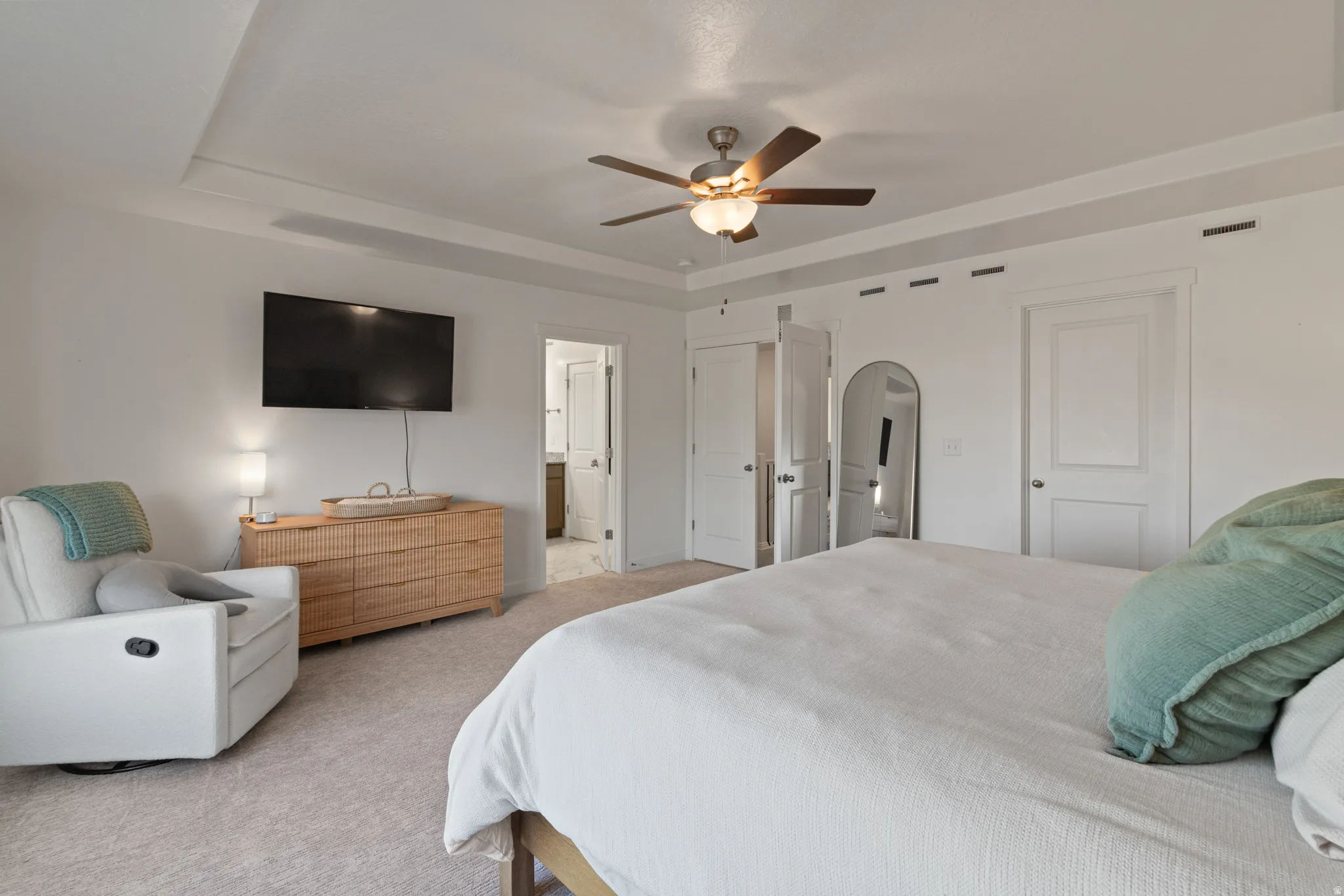 Bedroom featuring light colored carpet, a raised ceiling, a ceiling fan, and arched walkways