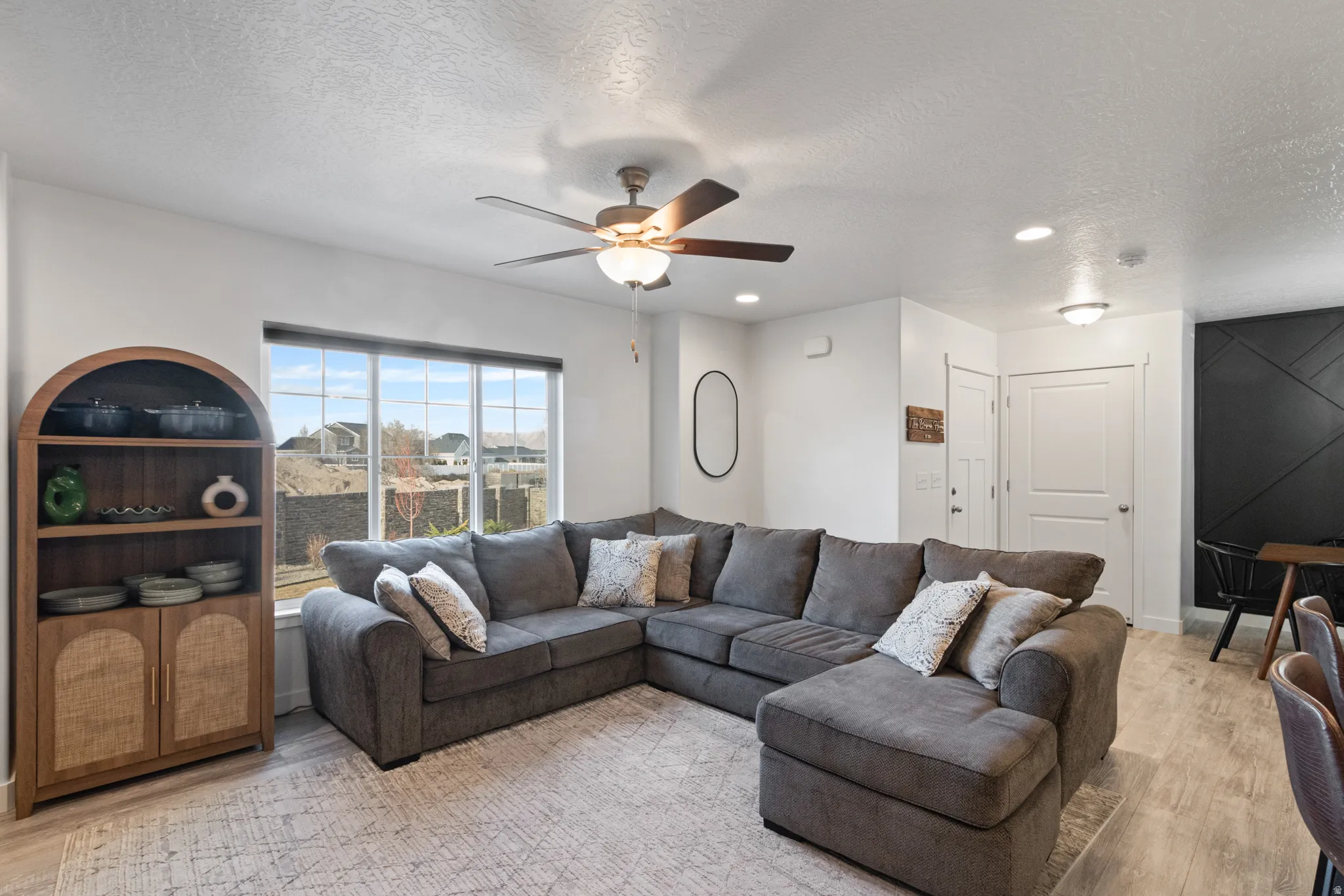 Living area with light wood-type flooring, a textured ceiling, a ceiling fan, and recessed lighting