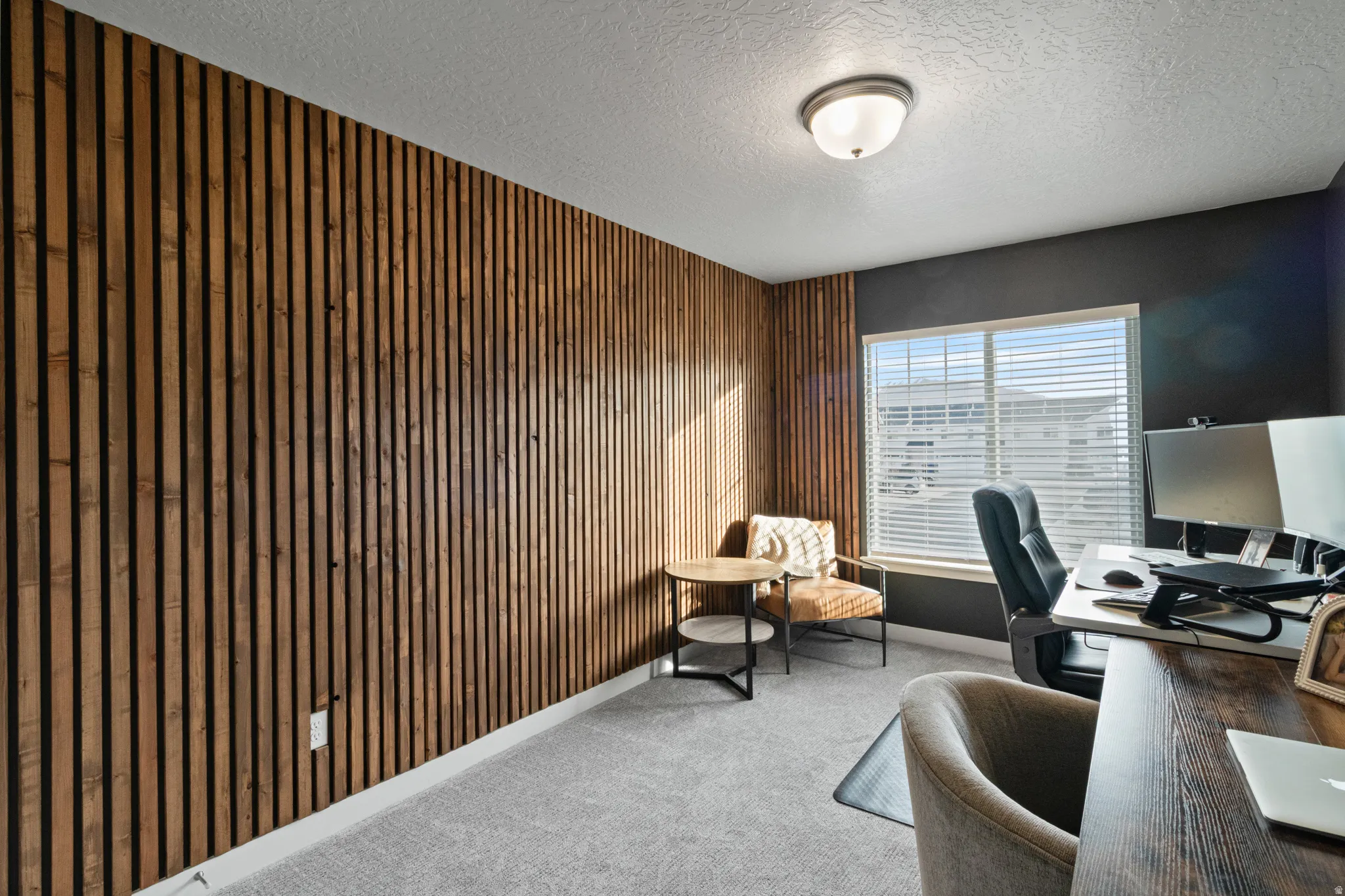 Office space with a textured ceiling, light carpet, and wood walls