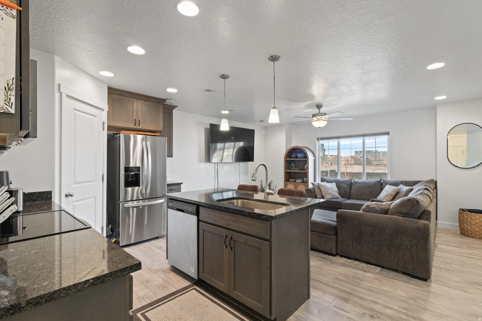 Kitchen with dark stone countertops, an island with sink, open floor plan, light wood-style floors, and stainless steel appliances
