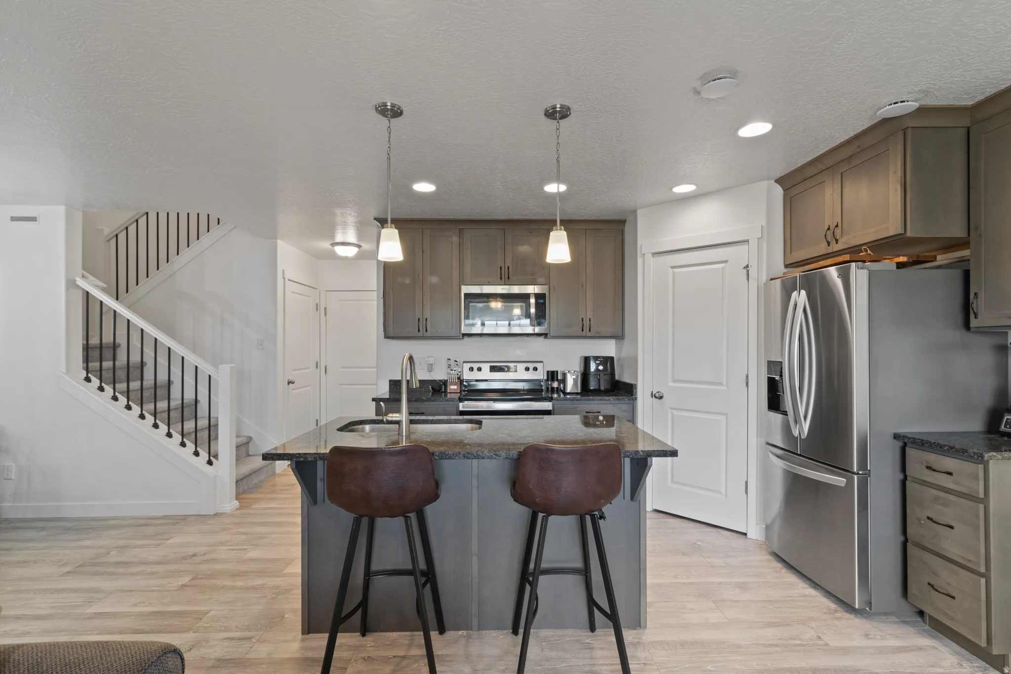 Kitchen featuring dark stone counters, light wood-style flooring, stainless steel appliances, a center island with sink, and a textured ceiling
