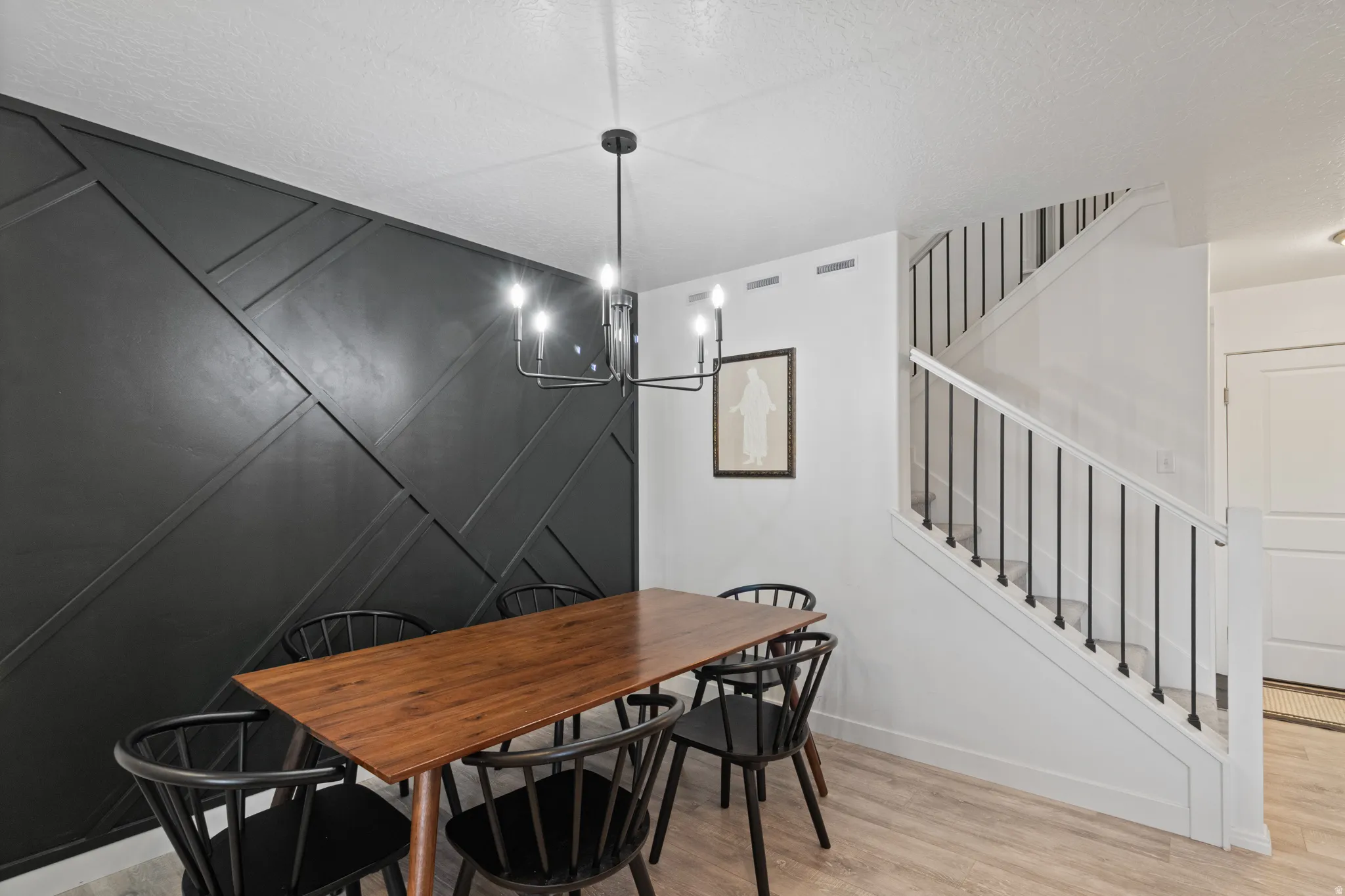 Dining room featuring light wood finished floors, a decorative wall, hanging lights, and a textured ceiling