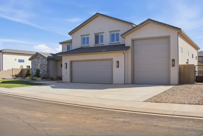 View of front of house with stucco siding, concrete driveway, an attached garage, and a gate