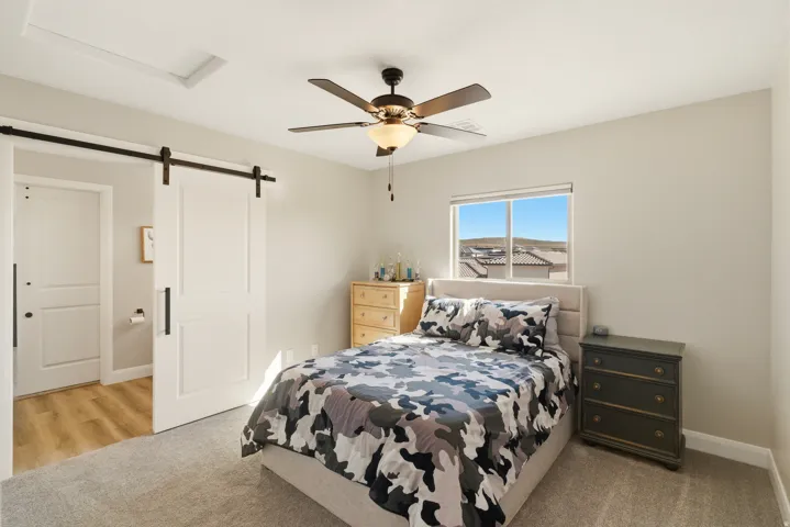 Bedroom with a barn door, ensuite bath, light carpet, and a ceiling fan