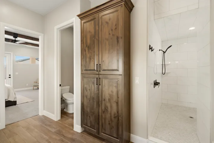 Ensuite bathroom featuring a shower stall, light wood-style floors, a ceiling fan, and beam ceiling