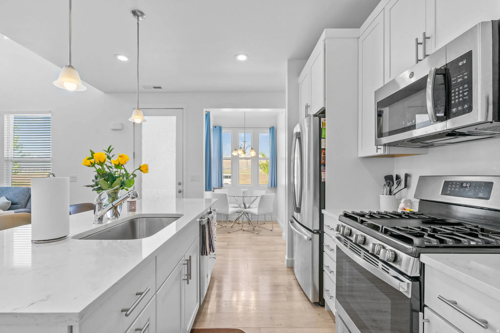 Kitchen featuring stainless steel appliances, light stone counters, white cabinets, light wood-style flooring, and a center island with sink