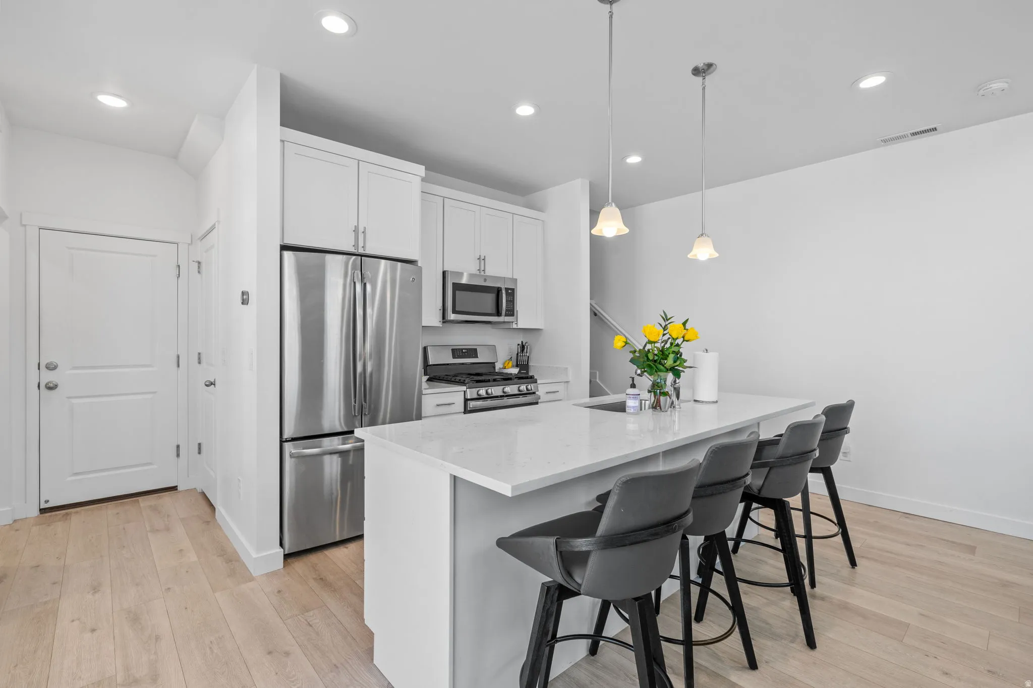 Kitchen with stainless steel appliances, a kitchen breakfast bar, light stone counters, an island with sink, and white cabinets