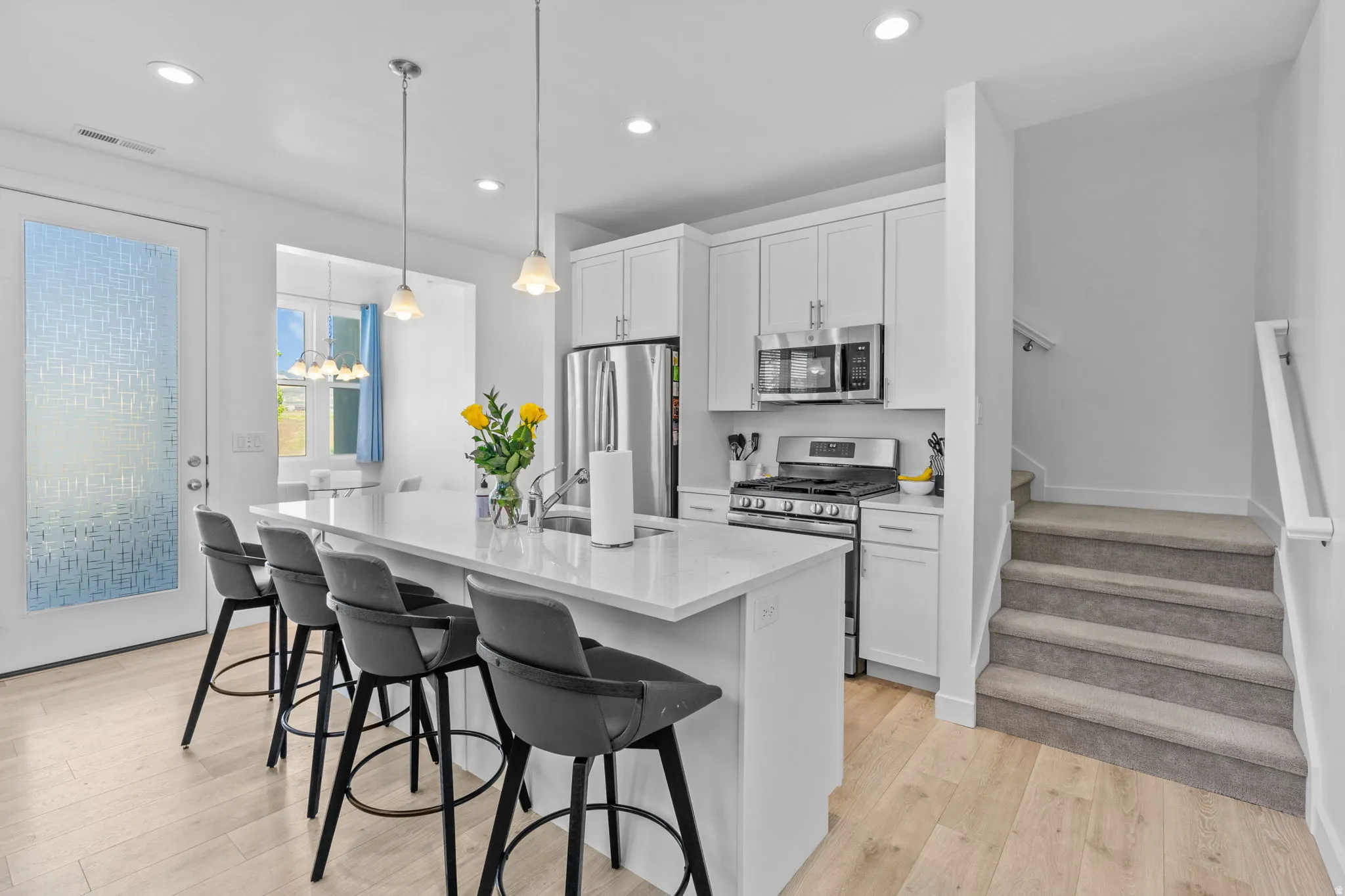 Kitchen featuring stainless steel appliances, a center island with sink, a breakfast bar area, white cabinets, and light wood-style floors