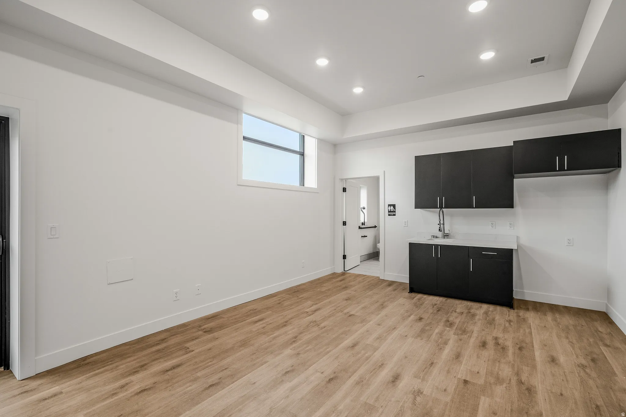 Bar with dark cabinetry, light countertops, recessed lighting, light wood-style floors, and a tray ceiling