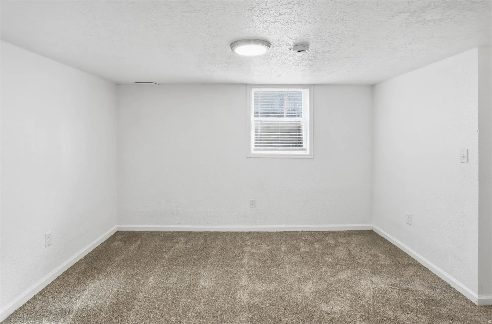 Carpeted spare room with a textured ceiling and a smoke detector