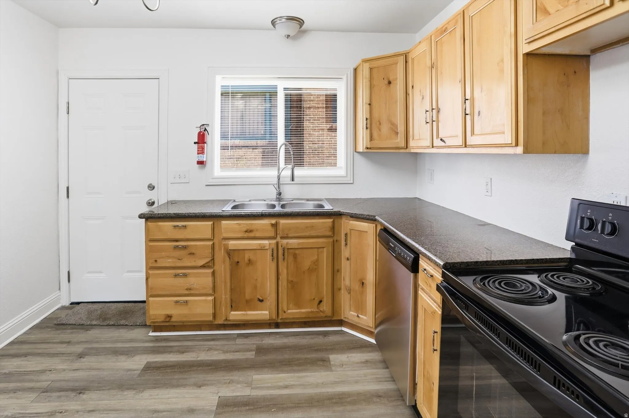 Kitchen featuring electric range, dark countertops, stainless steel dishwasher, light wood finish cabinetry, and light wood finished floors