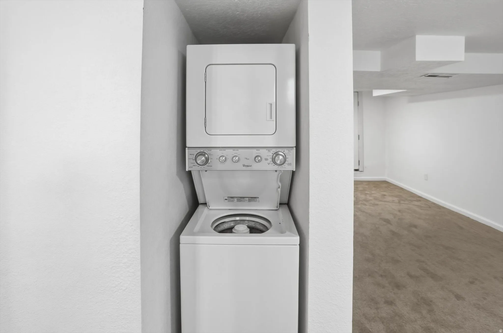 Laundry area with carpet floors, stacked washer / dryer, and a textured ceiling