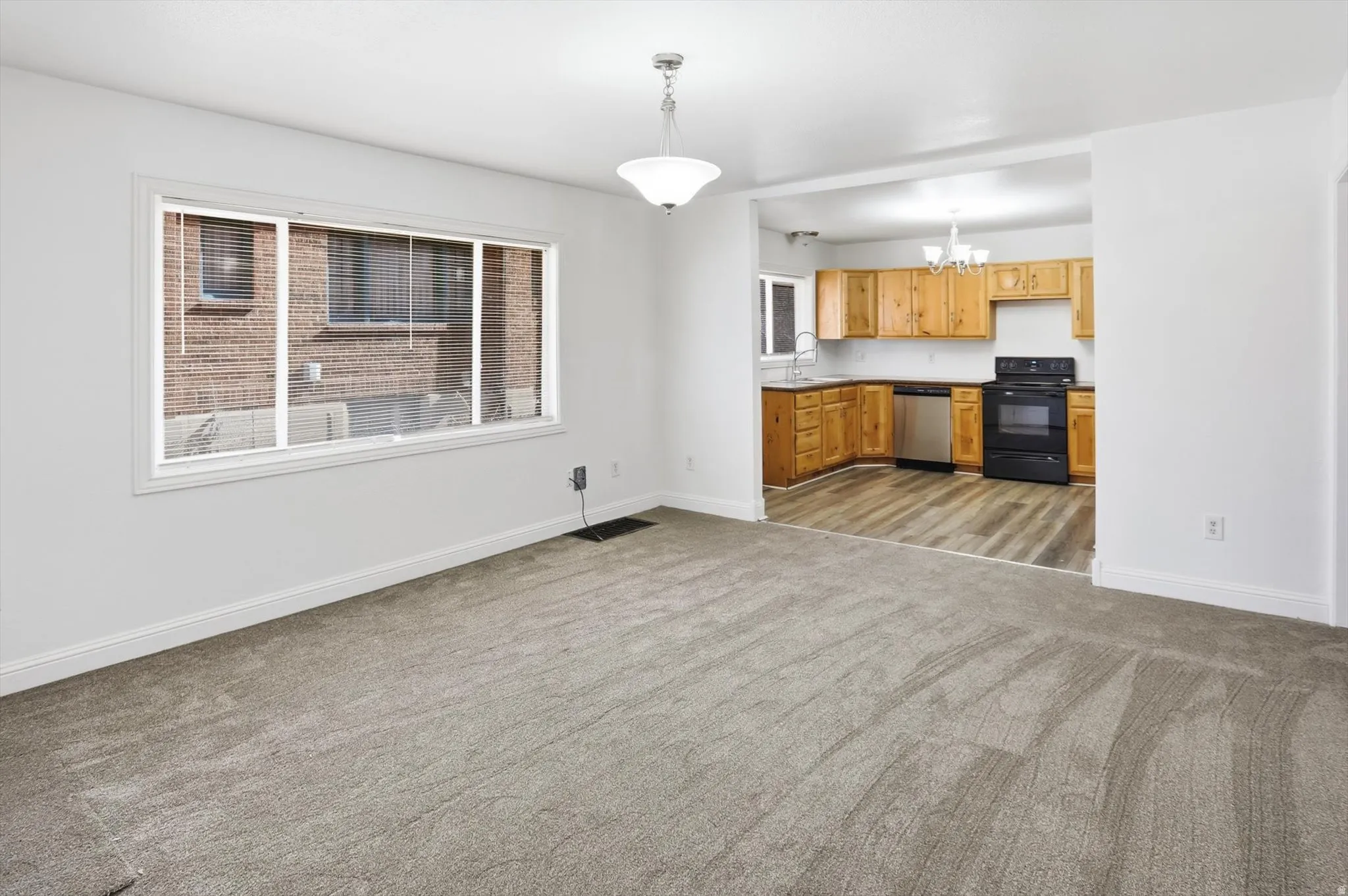 Kitchen featuring black / electric stove, dishwasher, hanging lights, light carpet, and open floor plan