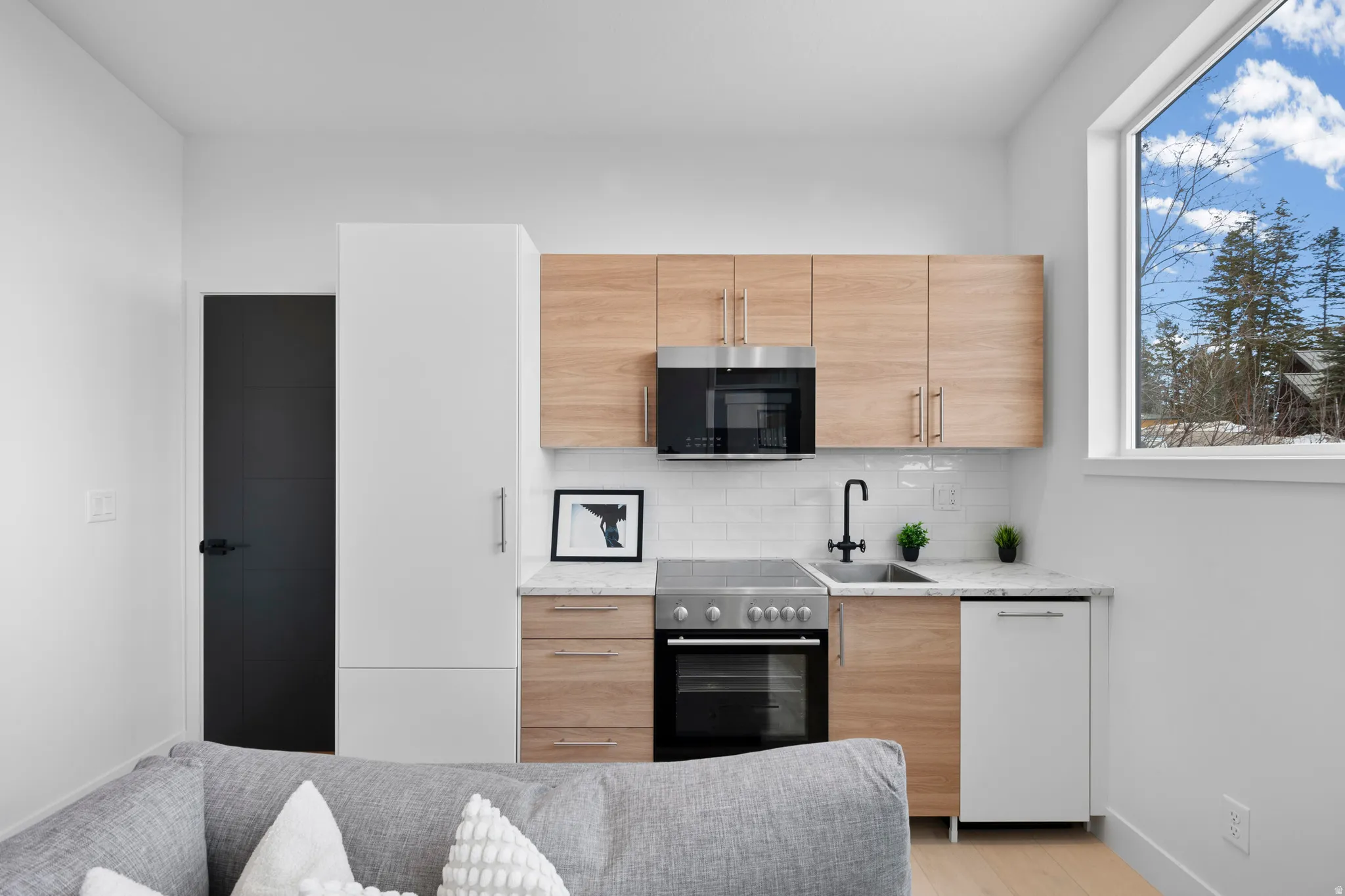 Kitchen featuring light wood finish cabinetry, modern cabinets, light stone counters, range with electric cooktop, and dishwasher