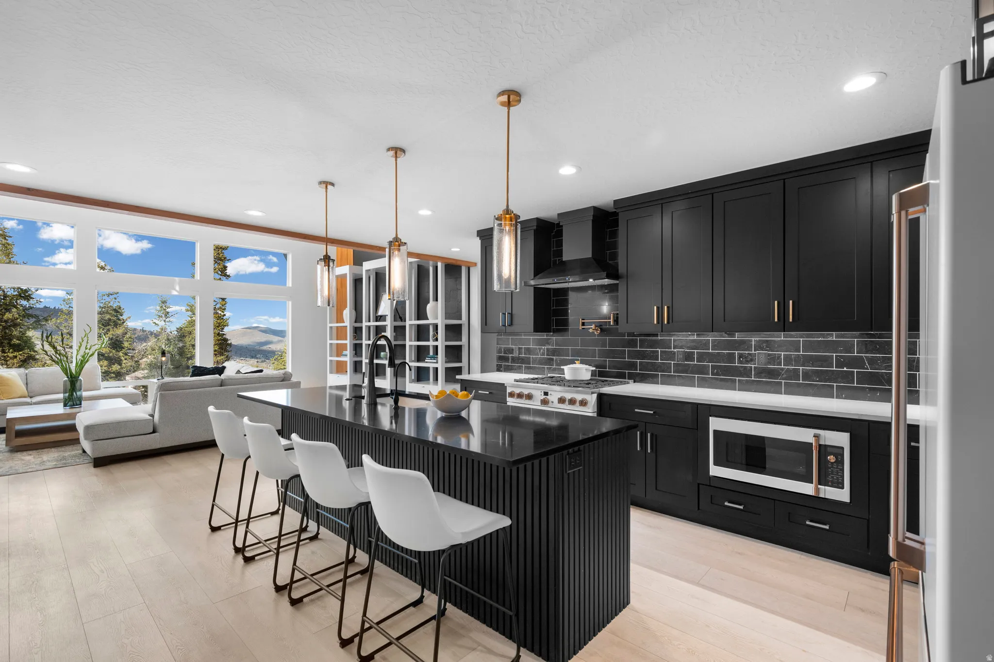 Kitchen featuring dark cabinetry, a center island with sink, a kitchen breakfast bar, dark stone countertops, and fridge