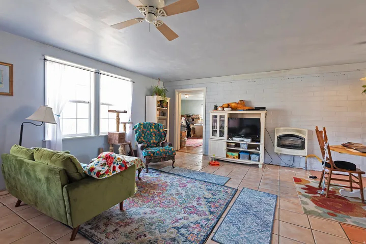 Living area featuring heating unit, light tile patterned flooring, ceiling fan, and brick wall