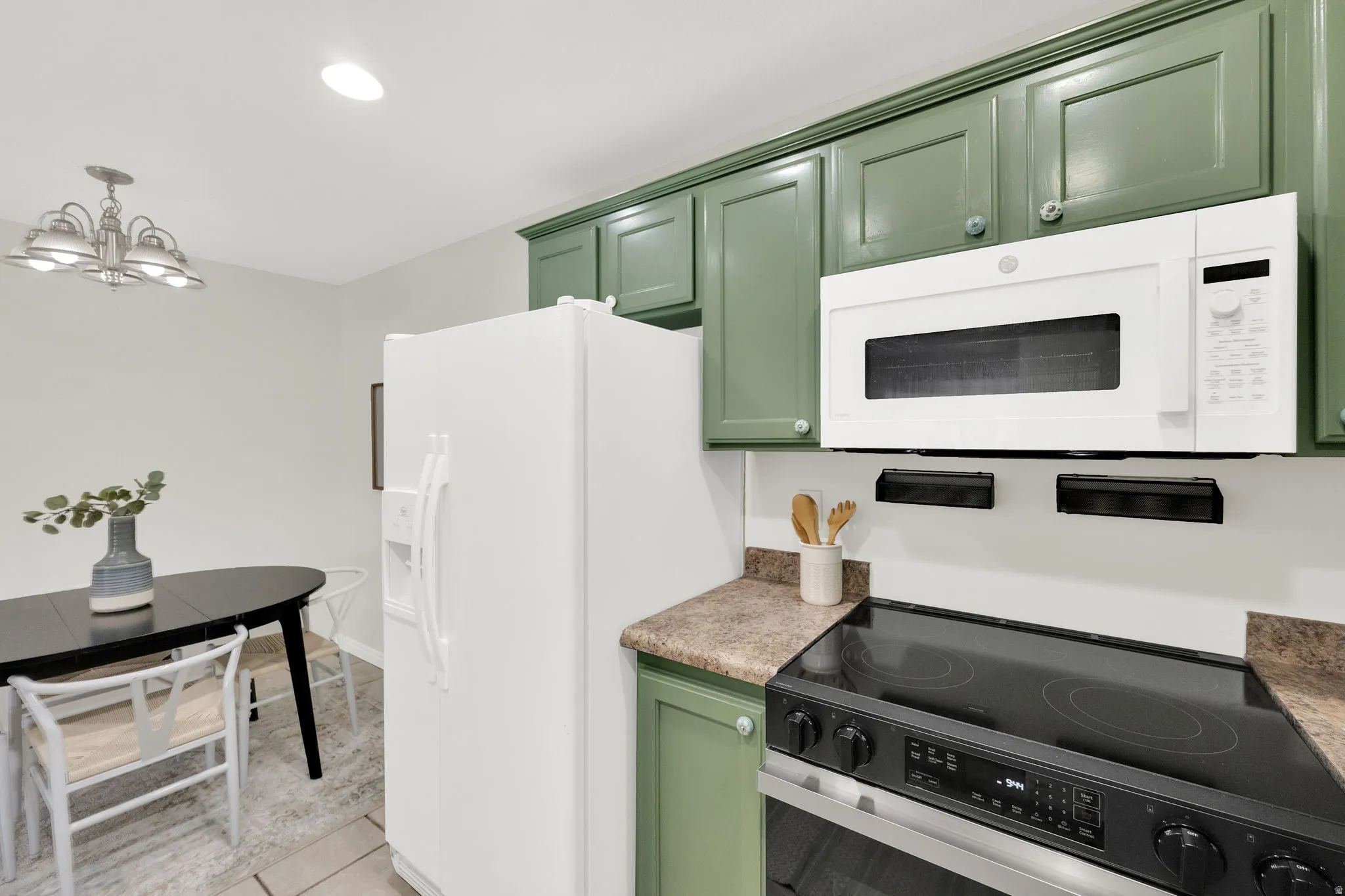Kitchen featuring green cabinetry, white appliances, hanging lights, light tile patterned floors, and light countertops