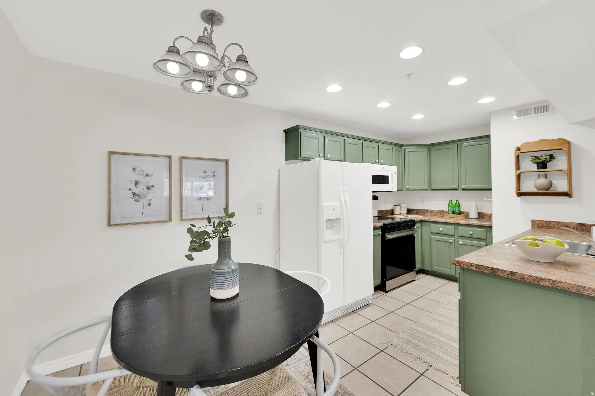 Kitchen with green cabinetry, white appliances, light tile patterned floors, light countertops, and hanging lights