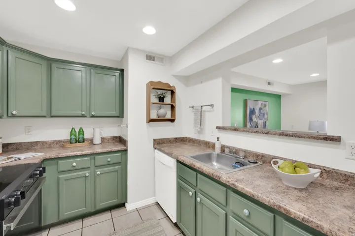 Kitchen featuring green cabinets, electric stove, dishwasher, light tile patterned floors, and light countertops